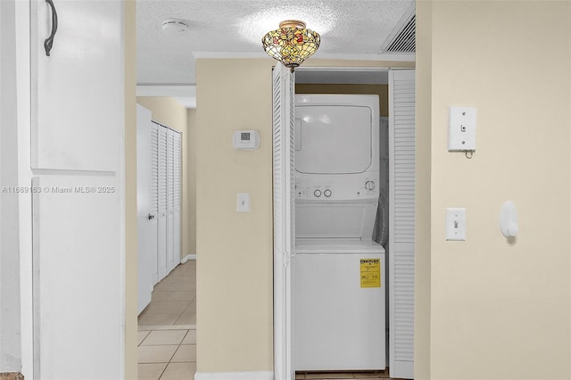 clothes washing area featuring stacked washing maching and dryer, a textured ceiling, and light tile patterned floors