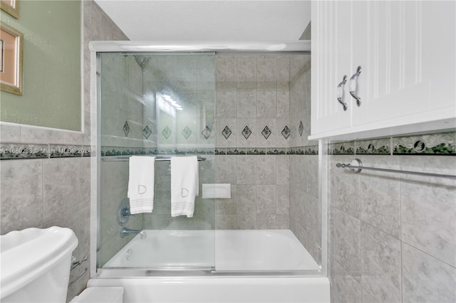 bathroom with toilet, tile walls, and bath / shower combo with glass door