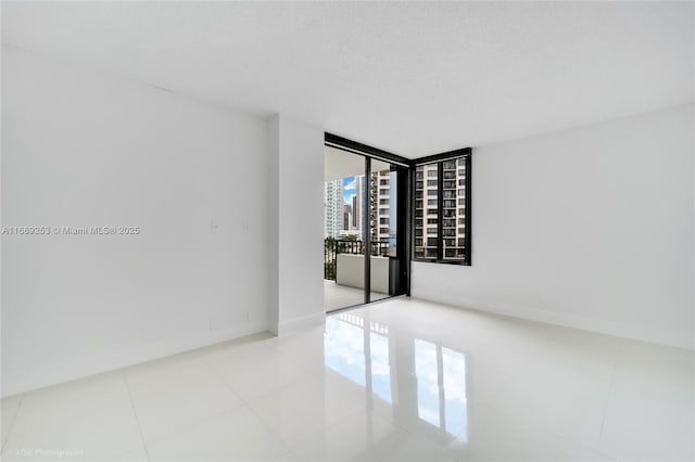 spare room with tile patterned floors, floor to ceiling windows, a textured ceiling, and baseboards