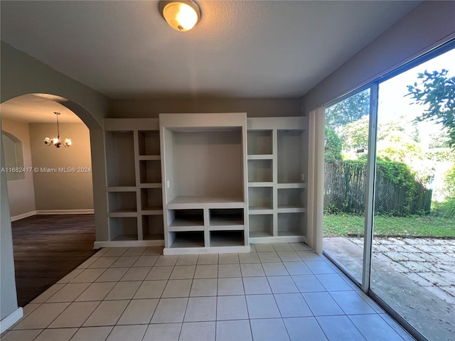 unfurnished living room featuring tile patterned flooring, a notable chandelier, and a textured ceiling