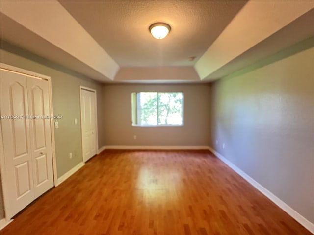 unfurnished bedroom with hardwood / wood-style floors, a textured ceiling, and a tray ceiling