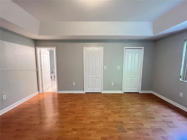 unfurnished bedroom featuring light wood-type flooring and two closets