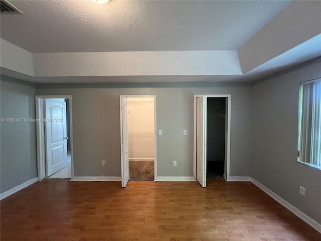 unfurnished bedroom with a textured ceiling, a spacious closet, hardwood / wood-style flooring, and a closet