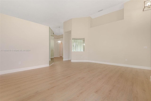 empty room with a towering ceiling, light wood-type flooring, and a notable chandelier