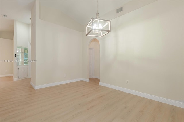 unfurnished room with light hardwood / wood-style floors, a notable chandelier, and lofted ceiling