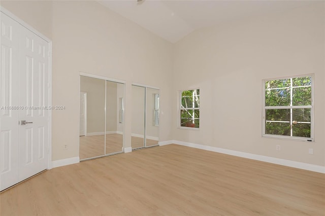 unfurnished bedroom featuring multiple closets, multiple windows, light hardwood / wood-style flooring, and high vaulted ceiling