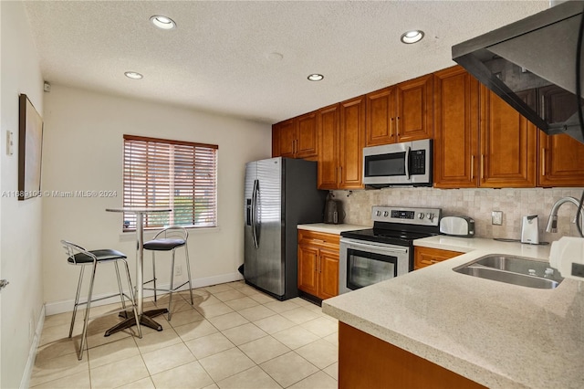 kitchen with appliances with stainless steel finishes, a textured ceiling, light tile patterned floors, decorative backsplash, and sink