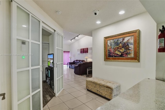 hallway with lofted ceiling, a textured ceiling, and light tile patterned flooring