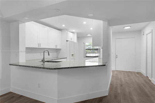 kitchen featuring sink, kitchen peninsula, dark stone counters, white fridge with ice dispenser, and white cabinets