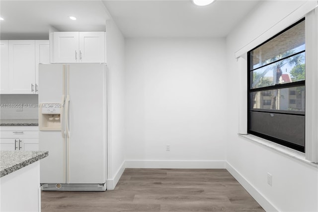 kitchen featuring light wood-type flooring, white cabinetry, white fridge with ice dispenser, and light stone counters