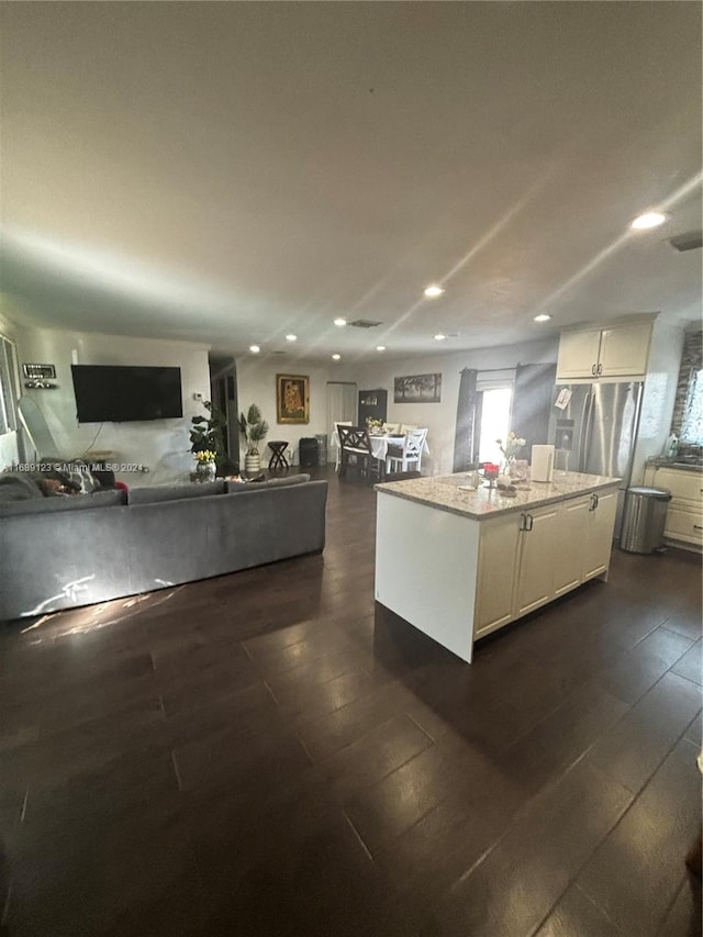 kitchen with white cabinets, dark hardwood / wood-style floors, a kitchen island, and light stone countertops