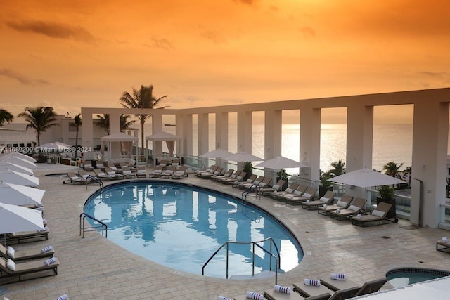 pool at dusk with a water view and a patio area