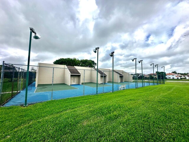 view of tennis court with a water view and a lawn