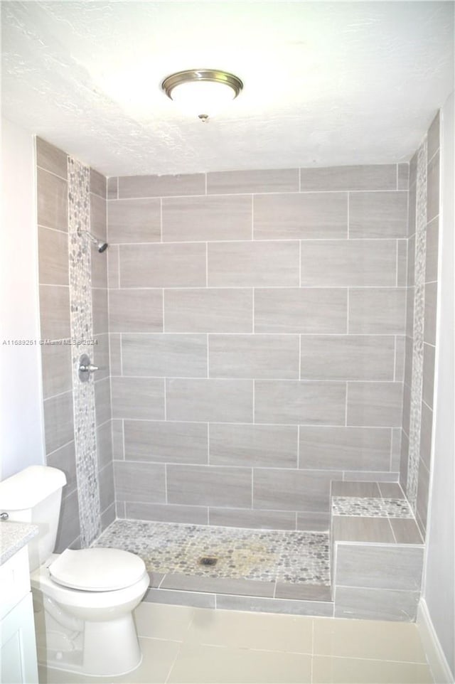 bathroom featuring toilet, vanity, tile patterned flooring, and tiled shower