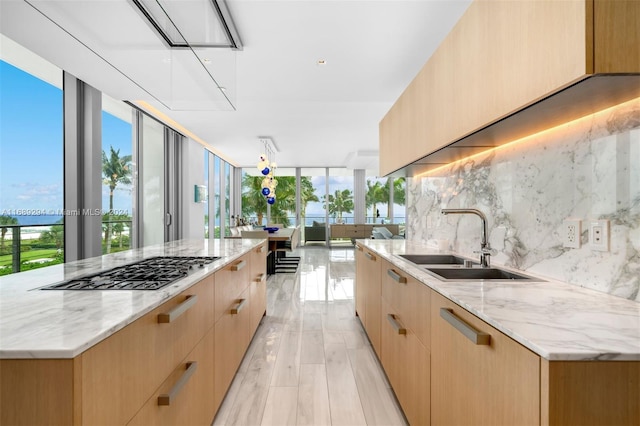 kitchen featuring a spacious island, sink, decorative backsplash, light hardwood / wood-style floors, and stainless steel gas cooktop