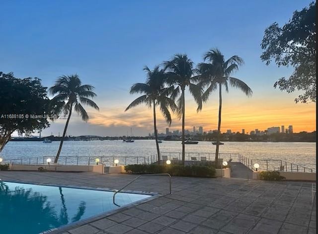 pool at dusk with a water view and a patio area