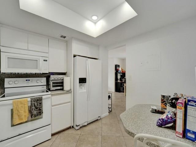 kitchen with white appliances, white cabinetry, and light tile patterned floors