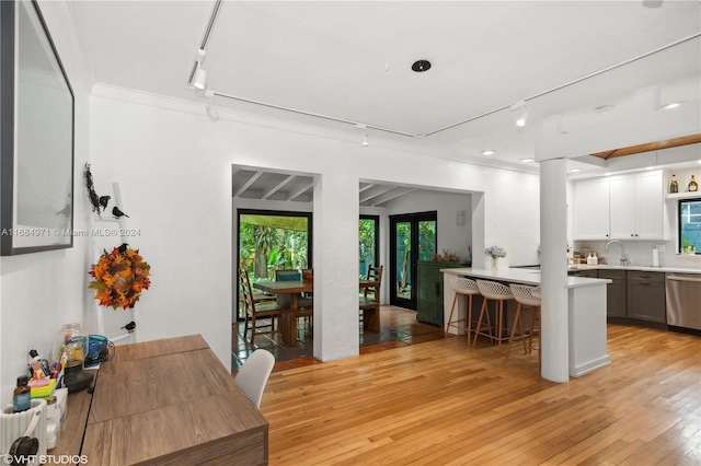 kitchen with white cabinetry, light wood-type flooring, sink, a kitchen breakfast bar, and dishwasher