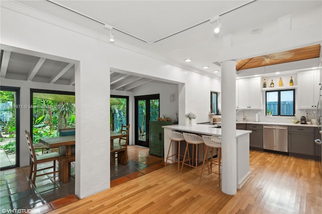 kitchen with white cabinetry, light wood-type flooring, a wealth of natural light, and stainless steel dishwasher