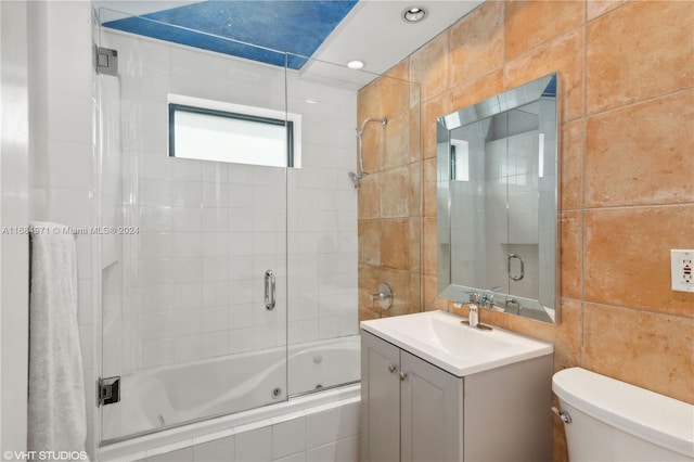 full bathroom featuring shower / bath combination with glass door, vanity, toilet, and tile walls