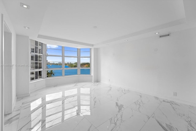 spare room featuring a tray ceiling and a water view