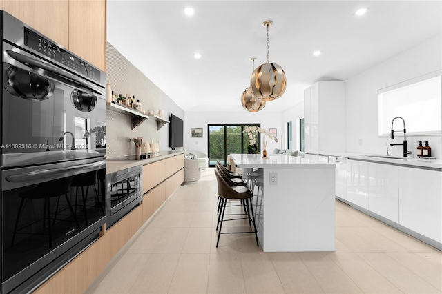 kitchen featuring a breakfast bar area, a kitchen island with sink, white cabinets, black double oven, and pendant lighting