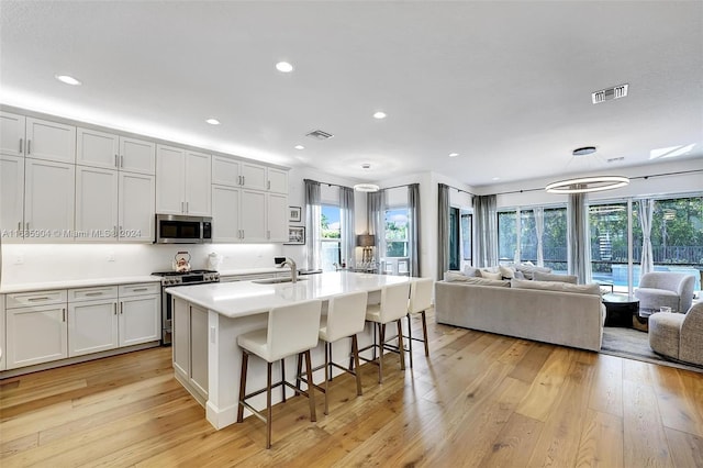 kitchen featuring white cabinets, appliances with stainless steel finishes, an island with sink, and light hardwood / wood-style flooring