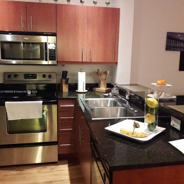 kitchen featuring light wood-type flooring, stainless steel appliances, dark stone counters, and sink