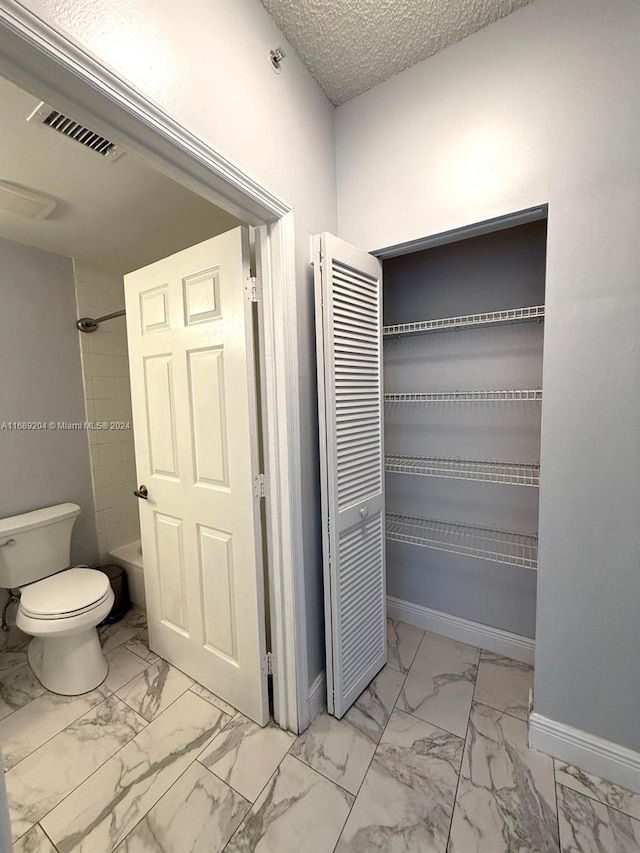 interior space featuring a textured ceiling, toilet, and tiled shower / bath