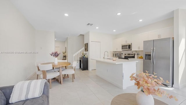 kitchen featuring white cabinetry, decorative backsplash, a center island with sink, light tile patterned flooring, and appliances with stainless steel finishes