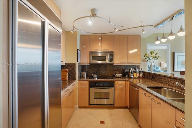 kitchen with stainless steel appliances, tasteful backsplash, hanging light fixtures, a sink, and dark stone countertops