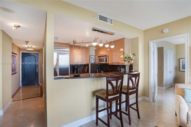 kitchen with appliances with stainless steel finishes, hanging light fixtures, decorative backsplash, dark stone countertops, and kitchen peninsula