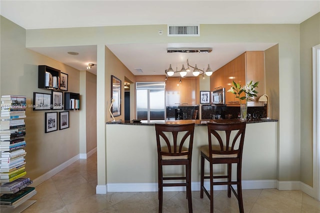 kitchen with stainless steel appliances, kitchen peninsula, a kitchen breakfast bar, pendant lighting, and decorative backsplash