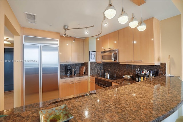 kitchen featuring appliances with stainless steel finishes, visible vents, dark stone countertops, and tasteful backsplash