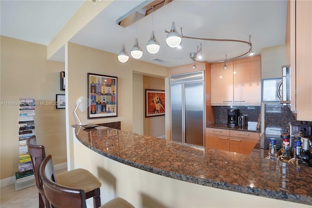 kitchen with stainless steel appliances, dark stone counters, pendant lighting, and kitchen peninsula