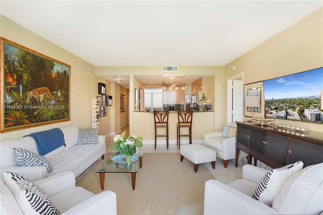 living area with light colored carpet, visible vents, baseboards, and an inviting chandelier