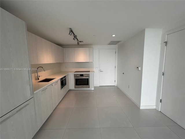 kitchen with track lighting, sink, stainless steel oven, and light tile patterned floors