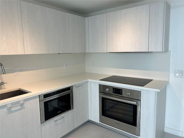 kitchen with black electric cooktop, stainless steel oven, sink, and light tile patterned floors