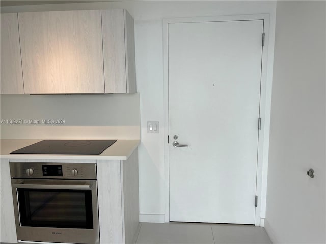 kitchen featuring stainless steel oven, light brown cabinets, light tile patterned flooring, and black electric stovetop