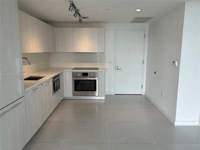 kitchen with stainless steel appliances, sink, track lighting, light brown cabinets, and light tile patterned floors