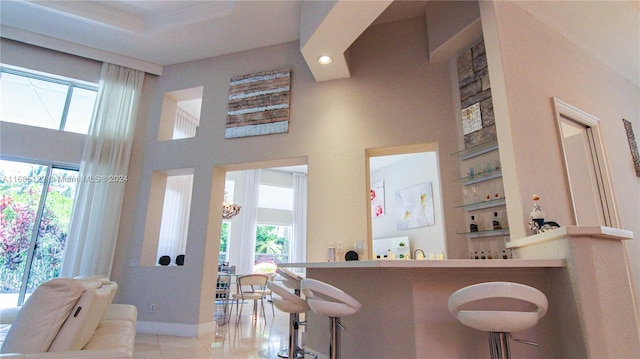 bar with light tile patterned flooring, a healthy amount of sunlight, and a towering ceiling