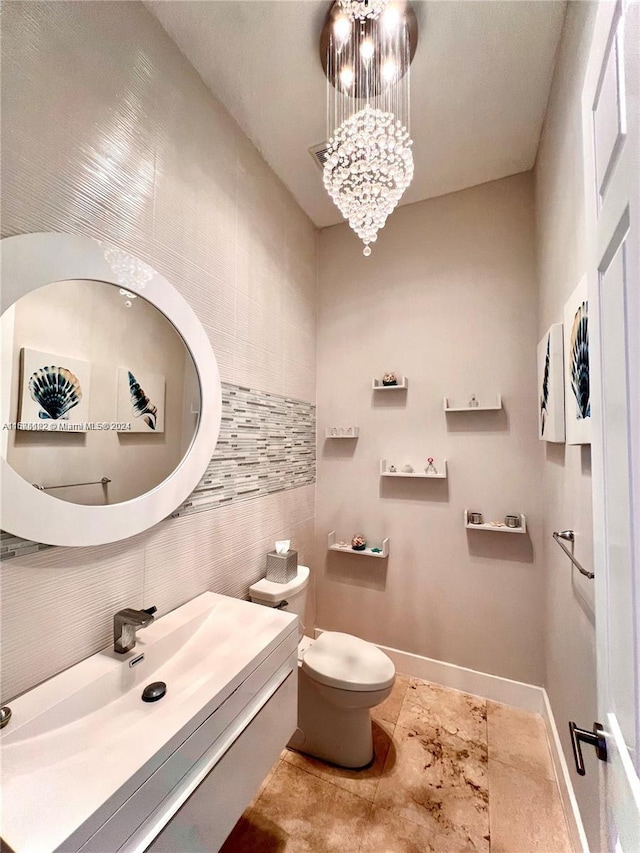 bathroom with an inviting chandelier, vanity, tile patterned floors, toilet, and tile walls