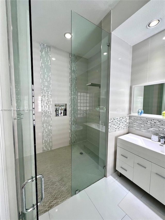 bathroom featuring a shower with door, tile walls, vanity, tile patterned floors, and decorative backsplash