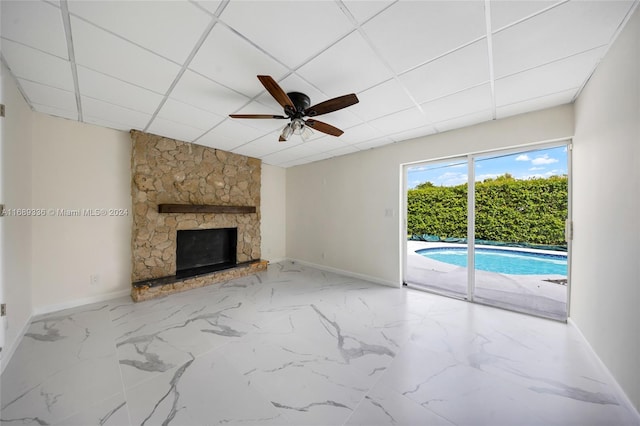 unfurnished living room with a fireplace, a drop ceiling, and ceiling fan