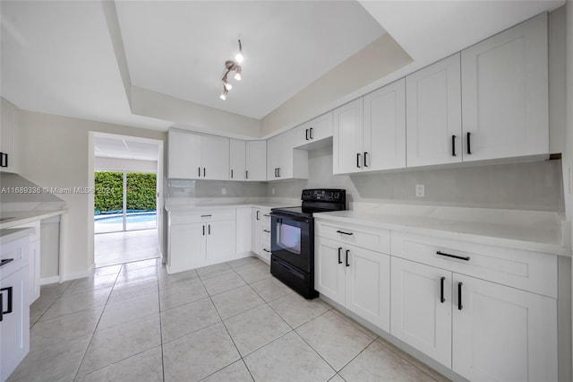 kitchen featuring a raised ceiling, light tile patterned floors, white cabinetry, and black range with electric cooktop