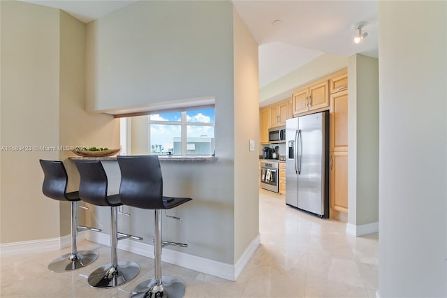 kitchen featuring light brown cabinets, light tile patterned floors, a kitchen breakfast bar, and stainless steel appliances