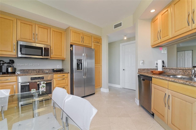 kitchen featuring stainless steel appliances, dark stone counters, light brown cabinetry, and sink