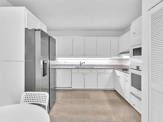 kitchen with a textured ceiling, white appliances, sink, light tile patterned floors, and white cabinetry