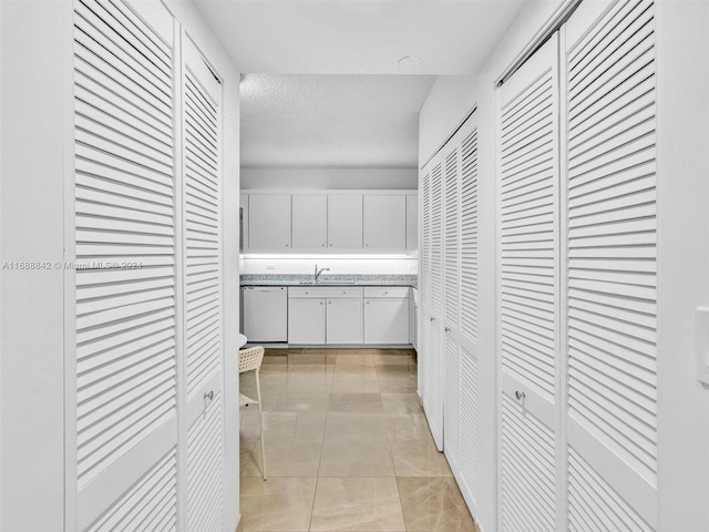 interior space featuring white dishwasher, sink, light tile patterned floors, a textured ceiling, and white cabinetry