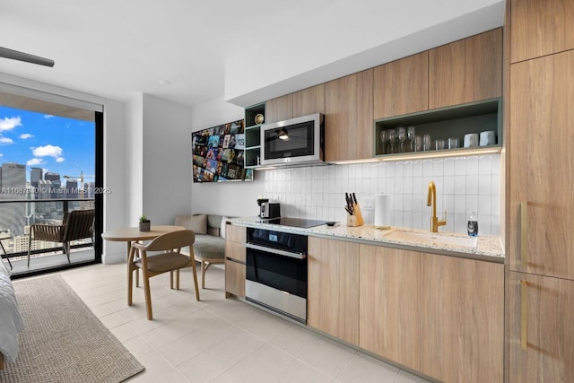 kitchen featuring sink, light stone countertops, expansive windows, oven, and decorative backsplash